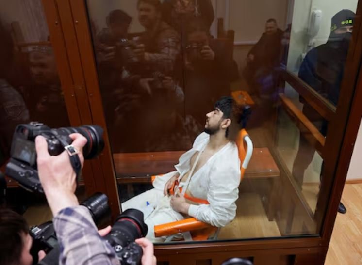 Muhammadsobir Fayzov, a suspect in the shooting attack at the Crocus City Hall concert venue, sits in a medical transport chair behind a glass wall of an enclosure for defendants before a court hearing at the Basmanny district court in Moscow, Russia March 24, 2024/REUTERS