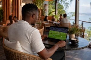 Man watching a football match on his laptop at a café 1xbet